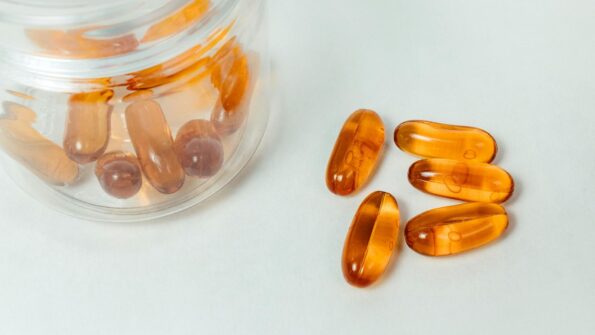透明药罐和散落的琥珀色维生素D软胶囊 — 象征年轻人补维D的简单方案